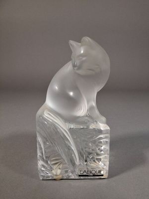 une figurine en verre représentant un chat assis sur un bloc
