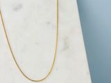 un collier à chaîne en or posé sur une dalle de marbre