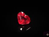 un gros plan d'un diamant rouge en forme de cœur sur une surface noire