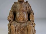 une statue en bois représentant un homme assis sur une chaise
