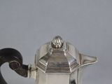 a silver tea pot with a handle on a table