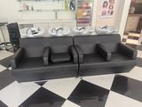 un sol à carreaux noirs et blancs dans un salon de coiffure pour hommes, équipé de trois lavabos et d'un canapé