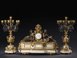 une horloge posée sur une table, à côté de trois chandeliers