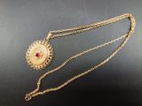 a close up of a gold necklace with a red stone on it