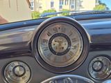 a clock on the dashboard of a car with a man in the background