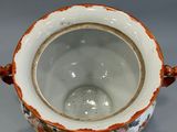 a white and orange vase with a handle on a table