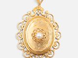 a close up of a gold pendant with a pearl in the center