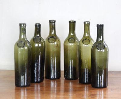 Six bouteilles de vin vertes sont alignées sur une table en bois