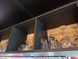 bottles and glasses on a shelf in a bar with a black ceiling