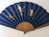 un éventail bleu orné d'oiseaux, accroché au mur