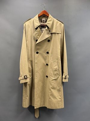 un trench-coat beige suspendu à un cintre devant un mur gris