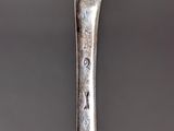 an old silver spoon sitting on top of a table next to a cup