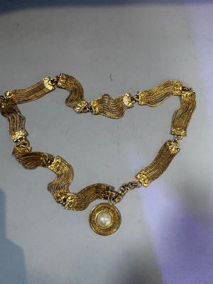 a close up of a gold necklace with a pearl on it