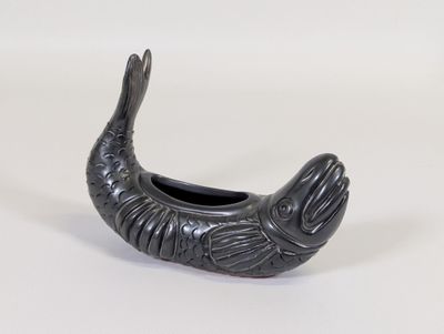 un petit récipient noir en forme de poisson posé sur une surface blanche