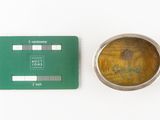 a small metal bowl with a yellow substance next to a green card