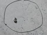 un collier en argent orné d'un diamant, posé sur une surface en béton