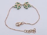 a close up of a gold bracelet with a green butterfly on it