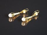 une paire de boucles d'oreilles en perles et en or posées sur un fond noir