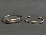 two silver bracelets on a table with a black background