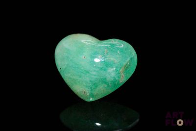 a close up of a green heart shaped stone on a black surface