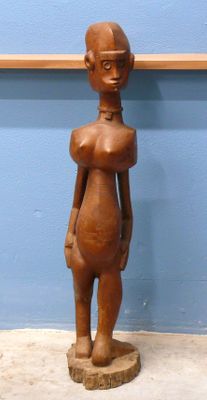 statue d'une femme debout sur un socle en bois, devant un mur bleu