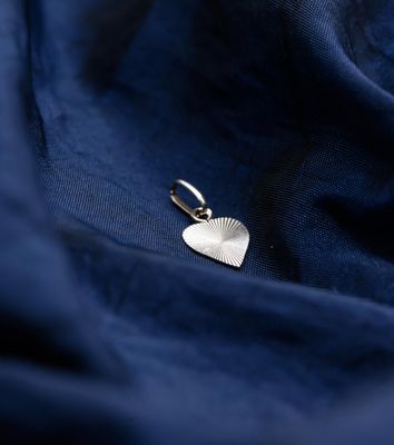 a close up of a silver heart charm on a blue fabric