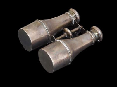 une paire de jumelles anciennes en argent sur fond noir, accompagnées de coupures de presse