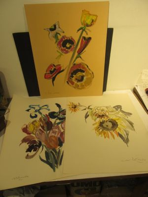 trois tableaux représentant des fleurs posées sur une table à côté d'une lampe