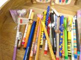 many pens and pencils in a wooden bowl on a table