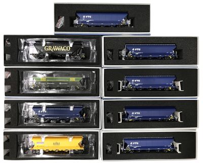 six wagons de train miniatures différents, présentés dans une vitrine posée sur un support blanc