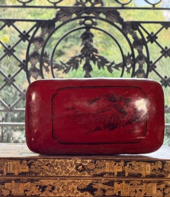 an old red box sitting on top of a table next to a window