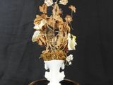 a white vase with dried flowers in it on a black table