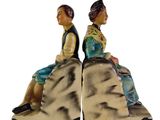 two figurines of people sitting on a rock with a white background