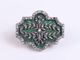 a close up of a green and silver broochle on a white surface