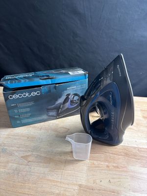an electric iron sitting on top of a wooden table next to a cup