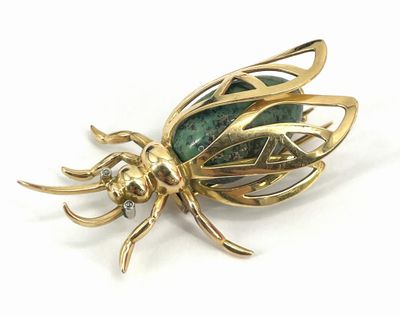 a close up of a gold insect broochle on a white background