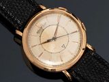 une montre-bracelet en or avec un bracelet noir posée sur un fond noir