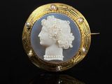 une image représentant une broche blanche et dorée ornée d'une tête de femme
