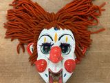 un masque de clown aux cheveux roux posé sur une table en bois