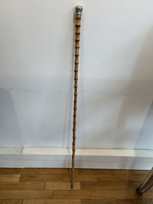 une vieille canne en bois avec un pommeau en métal posée sur un parquet