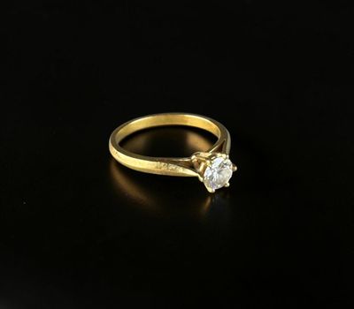 a gold engagement ring with a single diamond on a black surface