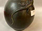 a black vase with a lizard on it on a white surface