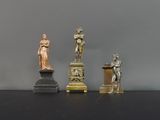 trois statues d'hommes et de femmes posées sur des socles, sur un fond noir