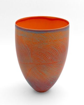 un vase orange et bleu posé sur une surface blanche