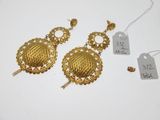 deux paires de boucles d'oreilles en or et une étiquette de prix posée sur une surface blanche