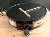 a crepe maker on a wooden table with a blackboard in the background