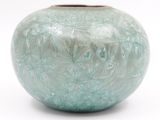 un vase vert posé sur une surface blanche, avec un fond blanc
