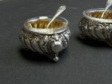 two silver bowls with spoons in them on a table
