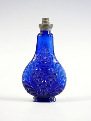 une vieille bouteille en verre bleu munie d'un bouchon en métal, posée sur une surface blanche