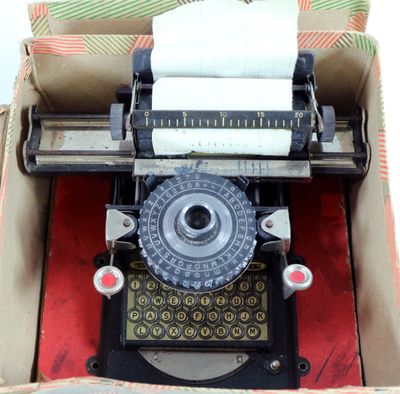 une vieille machine à écrire dans une boîte, sur laquelle est posé un rouleau de papier